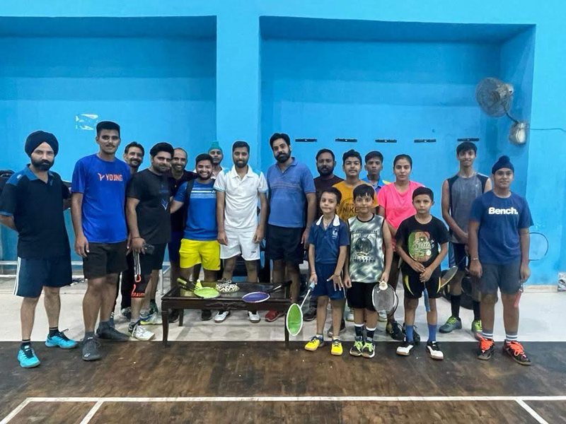 A large group of young players and Coach Suresh Kumar lined up on a badminton court
