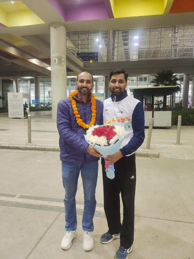 Raj Kumar, garlanded and holding flowers, beside Coach Suresh Kumar outside the airport terminal