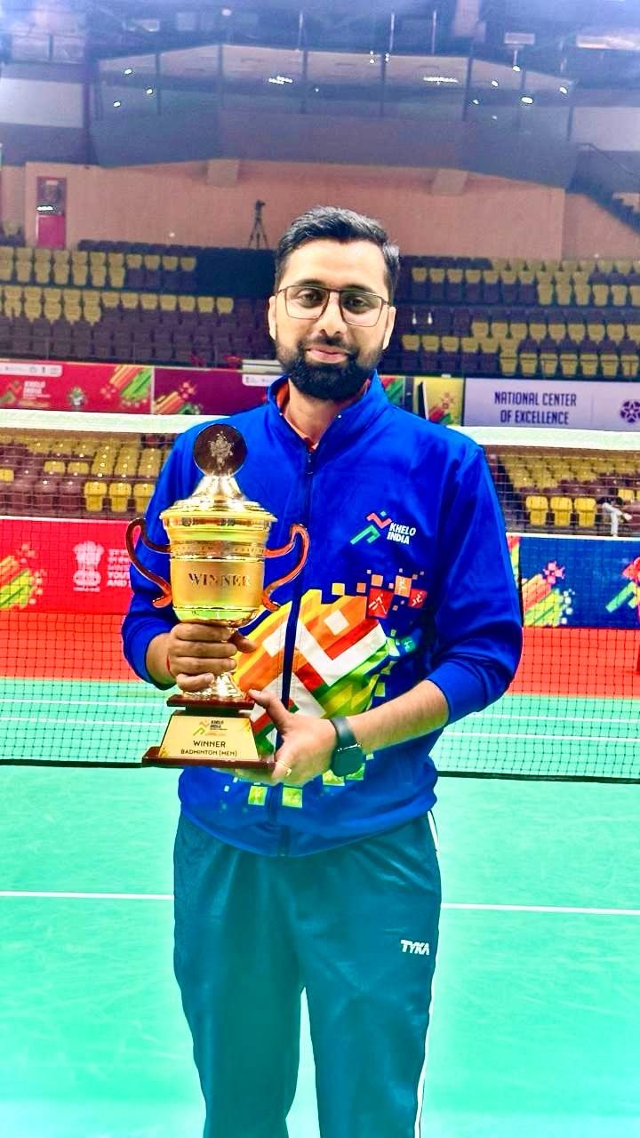 Suresh Kumar holding the Khelo India University Games trophy in a large indoor stadium